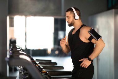 Spor salonunda koşu bandında çalışan kablosuz kulaklık takan yakışıklı erkek sporcu, spor yaparken müzik dinleyen Milenyum Erkek Sporcusu, kardiyo eğitiminin tadını çıkaran, uzay kopyalayan