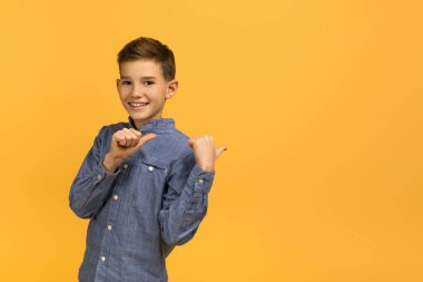 Harika bir teklif. Arkasındaki boşluğu işaret eden heyecanlı genç, iki başparmağı havada, mutlu bir genç erkek, sarı stüdyo arka planında tek başına dikilirken, panorama