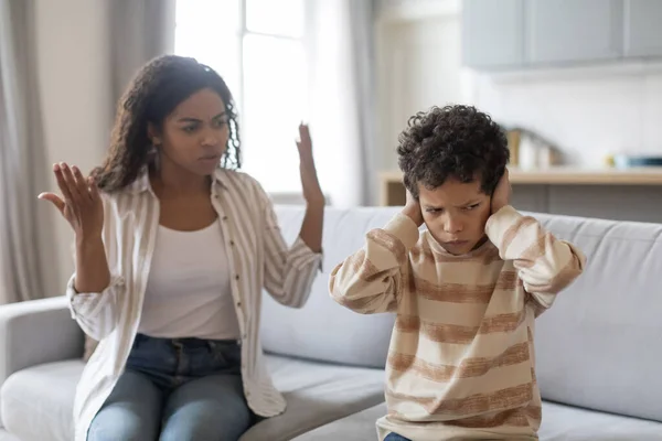 Family argument concept. Offended black boy covering ears, not to listen mothers scolding, young african american woman having fight with her child, quarelling at home, free space