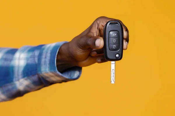 Closeup of black mans hand presenting set of car keys with remote, unrecognizable african american male suggesting ownership and mobility, standing isolated on yellow studio background, cropped