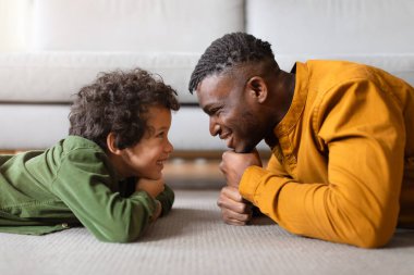 Siyahi baba ve oğlu yerde yüz yüze yatarken neşe ve neşe dolu, neşe dolu, neşe dolu, neşe dolu bir anı paylaşırken büyüleyici bir sahne beliriyor.