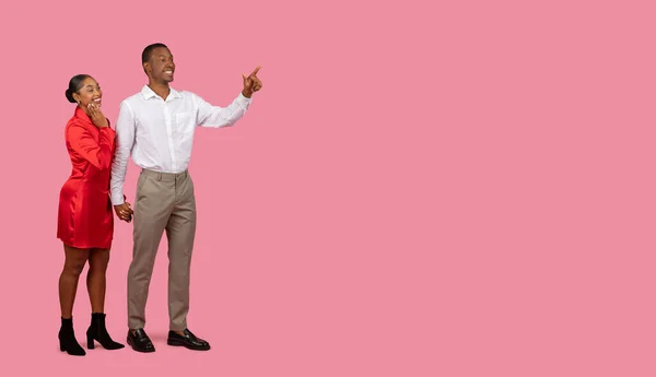 白いシャツの黒人男性 赤いドレスの女性と自由なスペースを指す笑顔と興味をそそる 広告のための場所 オファーやプロモーション ピンクの背景 — ストック写真