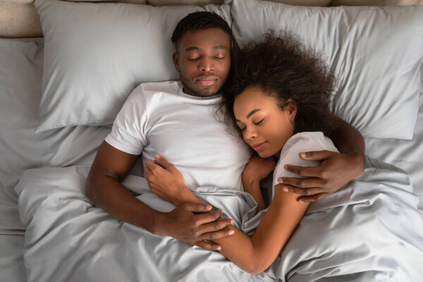 High angle view of affectionate african american spouses cuddling and hugging each other while sleeping in comfortable bed indoor. Overhead shot of loving young family embracing during night rest