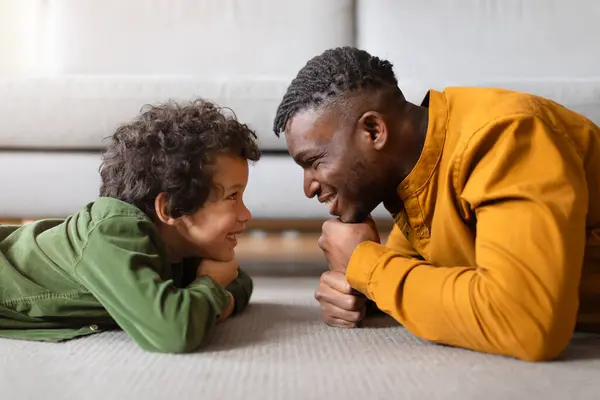 Siyahi baba ve oğlu yerde yüz yüze yatarken neşe ve neşe dolu, neşe dolu, neşe dolu, neşe dolu bir anı paylaşırken büyüleyici bir sahne beliriyor.