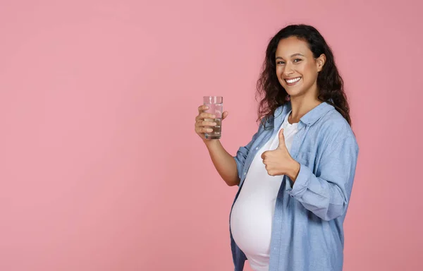 Těhotná Mladá Žena Drží Sklenici Vody Růžovém Pozadí Ukazuje Palec — Stock fotografie