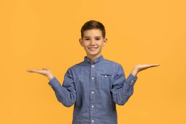 Seçim yap. Neşeli genç çocuk boş avuçlarıyla terazi yapıyor, mutlu genç erkek çocuk seçenekleri karşılaştırırken sarı stüdyo arka planında tek başına duruyor, boşluğu kopyalıyor.