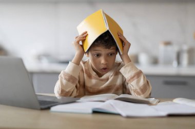 Evde eğitim sorunları. Ev ödevi yaparken kafasını kitapla örten siyah çocuk, masasında oturup kitap okuyan endişeli Afrikalı Amerikalı öğrenci, çalışmaktan yorulmuş, kapanmaktan bıkmış...