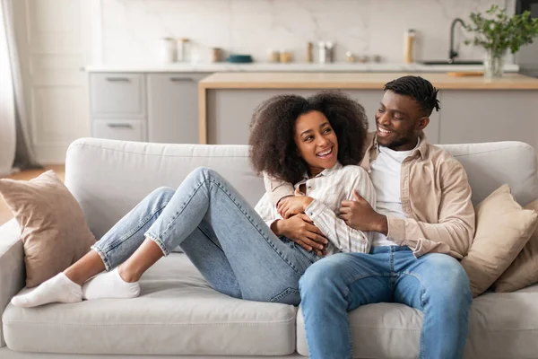 Home Comfort. Happy Loving Millennial Black Couple Chilling In Modern Living Room, Hugging While Resting Together On Weekend, Spending Free Time Cuddling In Cozy Stylish Interior