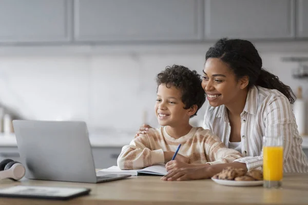 Remote Education. Black Mom And Little Son Using Laptop At Home Together, Happy Preteen Boy And His Beautiful Mother Looking At Computer Screen And Smiling, Enjoying Distance Learning Programs