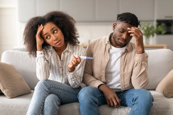 Unwanted Pregnancy. Upset Child Free African American Couple Holding Positive Pregnancy Test, Feeling Stressed Sitting On Couch At Home. Unplanned Childbirth, Unintended Pregnancies Concept