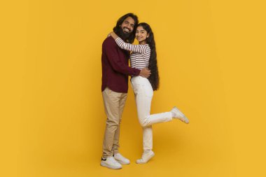 Aşk, sevgi, ilişkiler, Sevgililer Günü kutlaması. Mutlu milenyum Hindistanlı çiftin sarılıp kucaklaşması sarı stüdyo arka planında izole edilmiş, kameraya sarılıp gülümseyen, kopyalama alanı