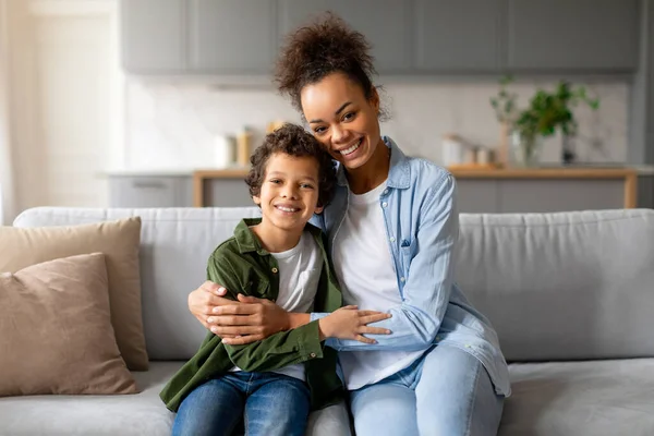 快乐的黑人妈妈拥抱着她十几岁的儿子 一头卷曲的头发 在家里舒适的沙发上享受着温暖的时光 — 图库照片