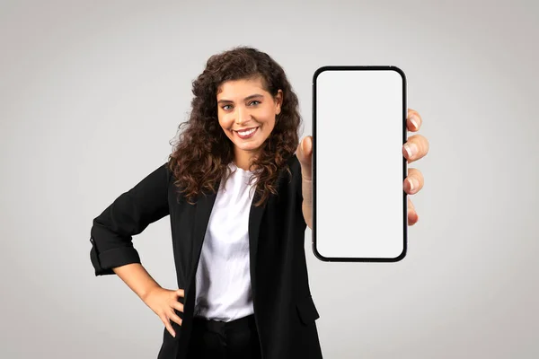在中立的背景下 穿着正装的女商人笑着 展示带有空白屏幕的手机 是商业模仿广告的理想场所 — 图库照片