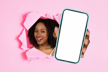 Mobil Reklam. Çekici mutlu siyah kadın cep telefonunu boş ekranla tutuyor, akıllı telefon cihazını pembe kağıt arka plandaki delikten gösteriyor, uygulamayı sunuyor. Kolaj