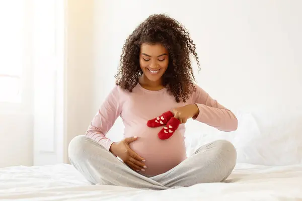 Negro Joven Madre Embarazada Sentada Cama Colocando Juguetonamente Calcetines Rojos —  Fotos de Stock