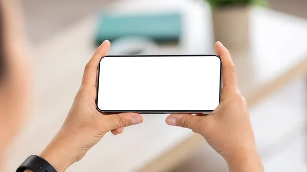 Mobile application, domestic entertainment concept. Smartphone with white blank template screen mockup copy space in woman hands, cropped of lady watching video content online