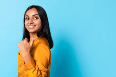 Teklifi kontrol et. Gülümseyen Orta Doğulu Kadın Başparmağıyla boşluğu işaret ediyor, Mavi Stüdyo Arkaplanına karşı poz veriyor, Mesajınızı ve afişinizi tanıtıyor,