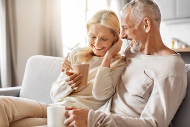 Güzel yaşlı adam ve kadın evlerinde birlikte vakit geçiriyorlar, rahat stüdyo dairede kanepede oturuyorlar, kucaklaşıyorlar, kahve içiyorlar, sohbet ediyorlar, gülüyorlar, yer kopyalıyorlar.