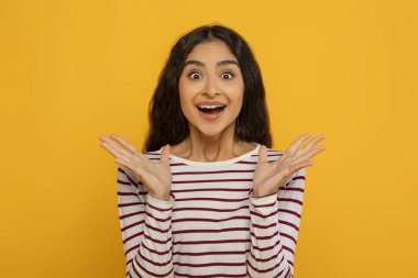 Şaşırtıcı derecede heyecanlı, uzun saçlı, el kol hareketi yapan, sarı stüdyo arka planında izole edilmiş olduğunu haykıran Hintli genç bir kadın.