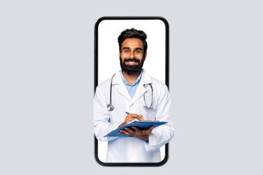 Sırıtkan orta yaşlı Hintli erkek doktor elinde akıllı telefon çerçevesiyle saklanmış bir pano tutuyor. Tarafsız arka plana karşı tele sağlık hizmetlerini sembolize ediyor.