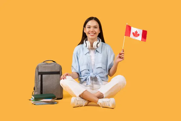 Veselá Mladá Studentka Držící Kanadskou Vlajku Sluchátky Kolem Krku Sedící — Stock fotografie