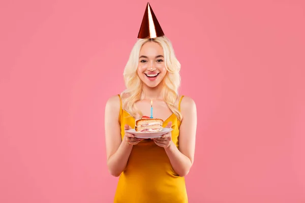 シックな黄色のドレスとパーティーの帽子で若い女性をビーイング 単一のろうそくで誕生日ケーキを開催 ピンクの背景に幸せを除く — ストック写真
