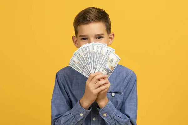 ドル紙幣のファン 現金で顔を覆う遊び心のある男性の子供の背後に隠れて 富や節約を象徴する黄色のスタジオの背景に立って スペースをコピー — ストック写真