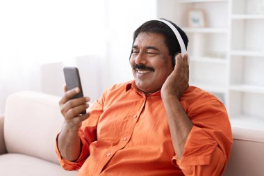 Bıyıklı, akıllı telefon ve kablosuz kulaklık kullanan, ailesiyle video görüşmesi yapan, internetten film izleyen, evdeki koltukta oturan, yer kopyalayan olgun Hintli adam. Dijital dünya