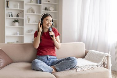 Gözleri kapalı neşeli Asyalı bir kadın. Kablosuz kulaklıkla müzik dinliyor. Neşeli Koreli bir kadın ritmi hissediyor.
