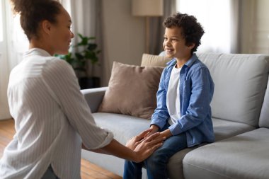 Gülümseyen siyah anne küçük oğluyla iç açıcı bir konuşma yaptı. Huzurlu oturma odasında gerçek bir bağ yarattı.