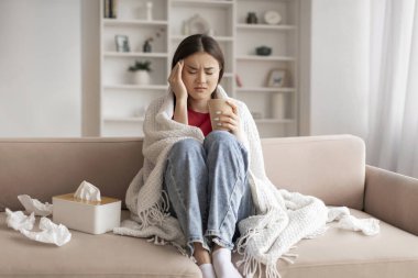 Battaniyeye sarılmış, evinde baş ağrısı çeken genç Asyalı hasta Koreli bir kadın kendini iyi hissetmiyor. Acı dolu bir ifadeyle kanepede oturuyor. Etrafı mendillerle çevrili.