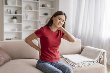 Genç Asyalı Kadın Evde Boyun ve Sırt Ağrısı Çekiyor, Koreli Hasta Kadın Ağrılı Bölgeleri Sürtünüyor, Kaşlarını çatıyor, Oturma odasında Kanepede Otururken Acıları Masaj Yapıyor, Boşluğu Kopyaladı