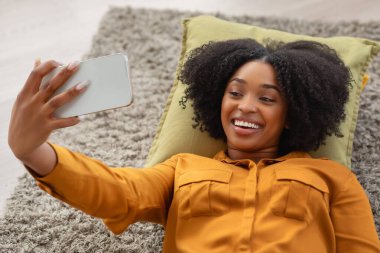 Neşeli, mutlu, binlerce yıllık Afro-Amerikan bir kadın canlı bir gülümsemeyle bir yastığın üzerinde uzanıyor, akıllı telefonuyla evde rahat, rahat bir şekilde selfie çekiyor, kapanıyor.