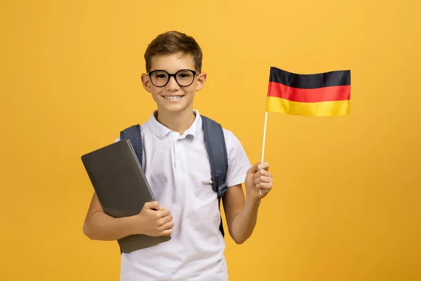 ハッピーティーンボーイの肖像画 バックパックホールドドイツの旗とラップトップ 笑顔ティーンエイジャーの学校のボーイ ポーズ イエロースタジオの背景 楽しい勉強 オンライン言語コースをお勧め コピースペース — ストック写真