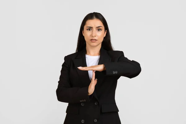 黒いスーツに焦点を当てた若いヨーロッパのビジネスマンは 彼女の手でタイムアウトサインを作り 深刻な表現を表示し 灰色の背景に立っています — ストック写真