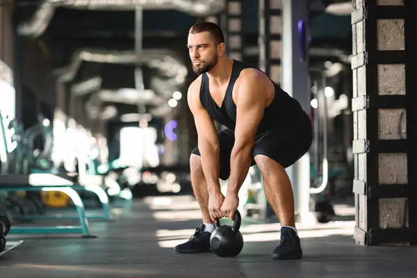 Motivated Muscular Man Training With Kettlebell At Modern Gym Interior, Young Handsome Bodybuilder Lifting Heavy Dumbbell While Exercising In Sport Club, Training Muscles, Copy Space