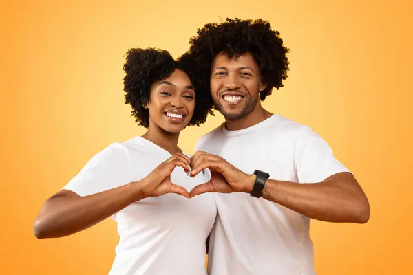 Valentines Day celebration concept. Loving young african american man and woman sweet cool millennial black couple embracing on colorful background, connecting hands, showing heart shaped gesture