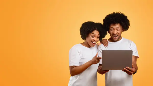 陽気なミレニアル世代のアフリカ系アメリカ人のカップルは 一緒にラップトップを使用してカジュアルな服を着て コンピュータ画面と笑顔 カラフルなスタジオの背景 コピースペース付きのパノラマを見ています オンラインショッピング — ストック写真