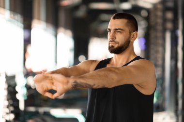 Spordan önce kollarını esneten yakışıklı bir erkek sporcu, kilit egzersizinde el ele tutuşuyor, genç kaslı vücut geliştirici bileklerini esnetiyor, egzersiz sonrası rutin soğutma hareketleri yapıyor.