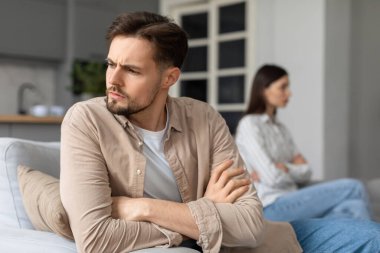 Kollarını kavuşturup, arka planda oturan bir kadına yan gözle bakan sorunlu genç bir adam kavga üstüne kavga ederek gergin bir ilişkiyi ima ediyor.