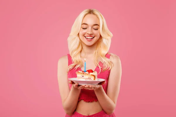 サンゴの上に満足した若いブロンドの女性 目を閉じて 誕生日のケーキにろうそくを吹き飛ばす前に瞬間を味わう ピンクの背景 — ストック写真