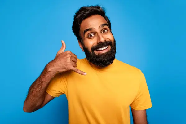 穿着黄色T恤的快乐的印度胡子男人叫我手势 在明亮的蓝色背景下显得热情而友善 — 图库照片