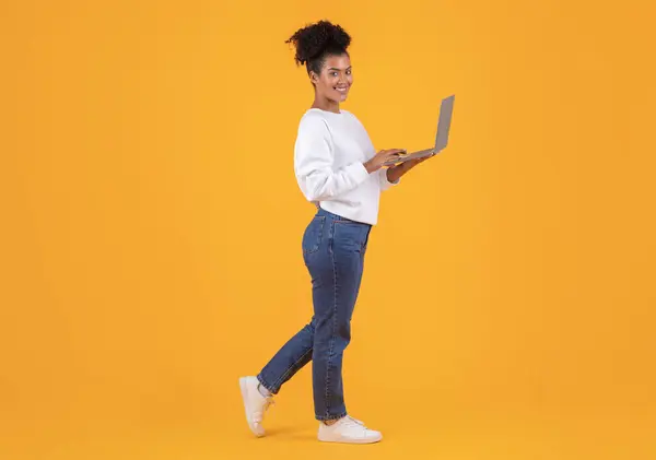 Portrait Of Young Smiling Black Woman With Laptop Computer In Hands Standing Isolated On Yellow Background, African American Female Working Online On Computer Or Browsing New Website,Copy Space
