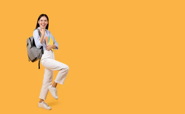 明るく陽気な女性学生 グレーのバックパックを保持するノートブック クレンチフィストと微笑み オレンジ色の背景 フル長さ 無料のスペースに対してポーズ — ストック写真