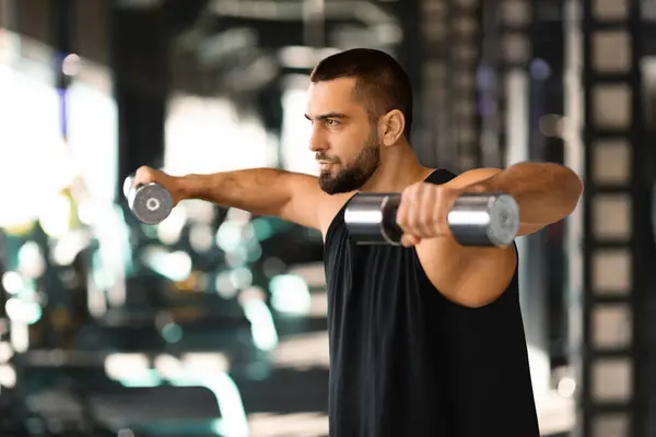 Young Muscular Man Doing Dumbbell Lateral Raise Exercise At Gym, Motivated Male Athlete Training Muscles At Modern Fitness Club, Lifting Light Weights, Enjoying Bodybuilding Workout, Free Space