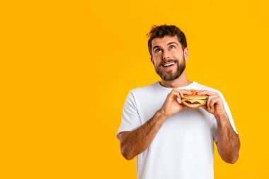 Sarı arka planda fotokopi alanının yanında çizburgerin tadını çıkaran aç bir adam, rüya gibi bir ifadeyle yukarı bakıyor, diyet yerine zevk anının tadını çıkarıyor, abur cubur şeytana teslim oluyor.