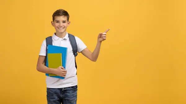 バックパックと教科書を運ぶハッピースクールボーイとコピースペース 陽気な10代の男性の子供は 明るい黄色の背景 パノラマに立って方向や選択を示唆しています — ストック写真