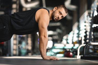Odaklanmış sakallı adam spor salonunda antrenman yaparken yerde şınav çekiyor. Yakışıklı kaslı erkek sporcu yoğun egzersiz sırasında kararlılık ve güç gösteriyor.