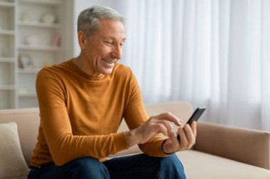 Akıllı telefon kullanan, kaydıran, web sörfü yapan, evdeki koltukta oturan, reklam için boş alanı kopyalayan yakışıklı, gri saçlı son sınıf öğrencisi. Yaşlılar için mobil başvuru