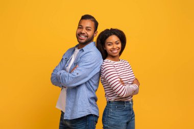 Sarı arka planda poz veren neşeli siyahi erkek ve kadın portresi, mutlu Afrika kökenli Amerikalı erkek ve kadın kollarını kavuşturmuş kameraya gülümsüyor,